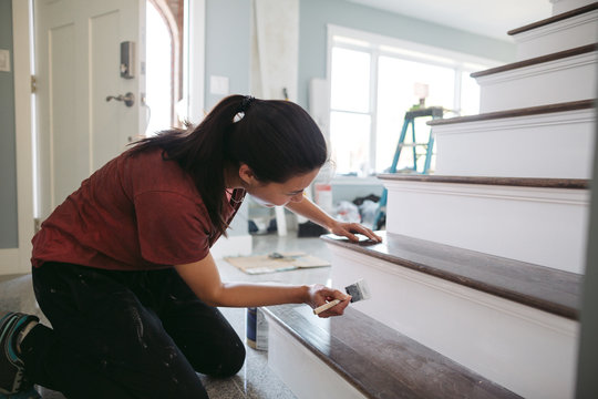 Young woman painting house trim inside.