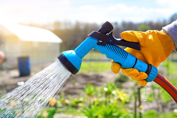 Watering the garden with watering hose and spray gun in a hand