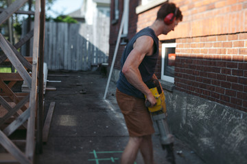 Young man breaking up concrete with jack hammer