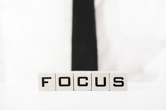 Businessman with sign Focus spelled on white wooden blocks on the table in front of him