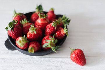 Fresh juicy strawberries in a black plate on a white background