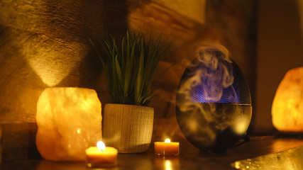 Electric oil diffuser lamp, candles on wooden table in room.