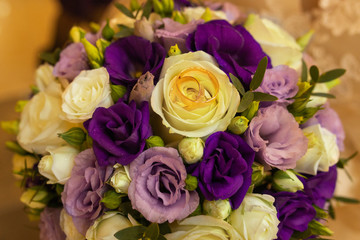 Gold wedding rings on a wedding bouquet of yellow and purple roses. Close-up. Wedding
