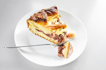 piece of cake baked with cottage cheese and cherry on a white plate with a spoon.