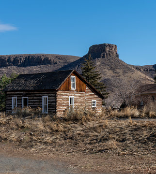 Old Wooden Log Cabin with High Desert Mesa in Background Against a Clear Blue Sky
