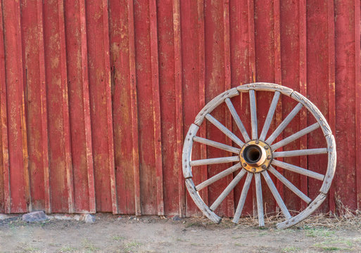 Old, Faded, Western, Wooden Wagon Wheel Leaning Against Red Barn (horizontal format)