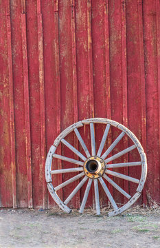 Old, Faded, Western, Wooden Wagon Wheel Leaning Against Red Barn (Vertical format)