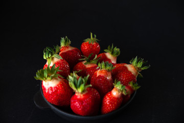 Fresh juicy strawberries in a black plate on a black matte background