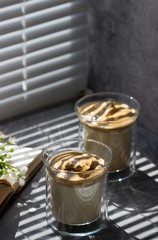 Dalgona Coffee in transparent glasses on a windowsill illuminated by sunlight.