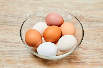 eggs of different colors in a glass bowl on a wooden table surface