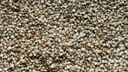 Background from raw organic green buckwheat porridge, vegan food. Texture of scattered buckwheat groats. Seeds are triangular in shape. Organic food. The concept of diet, weight loss, healthy eating