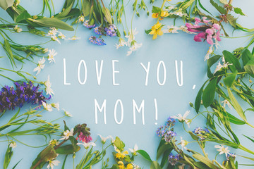 Love you Mom! Happy Mother's day greeting card. Heart of colorful spring flowers on blue background flat lay with greeting text. Floral greeting card. Happy Mothers day stylish flat lay