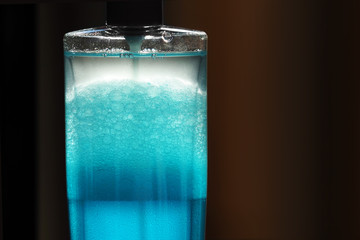 Blue gel and bubbles in a clear plastic bottle on dark background. Multilayer liquid, cosmetical...