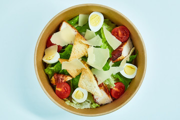 Salad with chicken, cherry tomatoes, lettuce, quail eggs, parmesan cheese, white bread crackers in a cardboard box