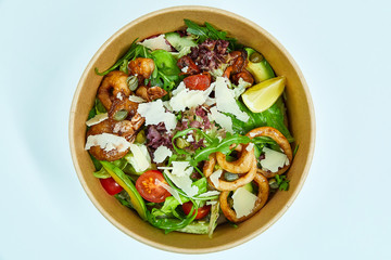 Seafood salad with grilled shrimps, mussels, squid rings, lettuce, cherry tomatoes, Parmesan cheese, capers, avocado and a slice of lemon in an artichoke box