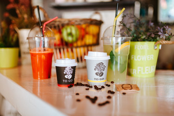 Close up of two takeaway coffees, refreshing juices and coffee beans on the table