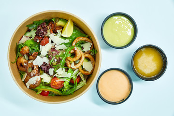 Seafood salad with grilled shrimps, mussels, squid rings, lettuce, cherry tomatoes, Parmesan cheese, capers, avocado and a slice of lemon in an artichoke box