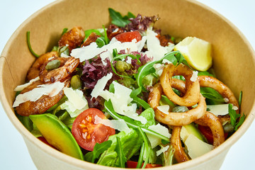 Seafood salad with grilled shrimps, mussels, squid rings, lettuce, cherry tomatoes, Parmesan cheese, capers, avocado and a slice of lemon in an artichoke box