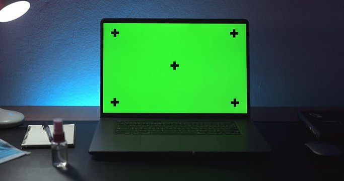 Zoom out from Green screen Mock-up laptop computer with mask and sanitizer on desk in night room with ambience colorful light