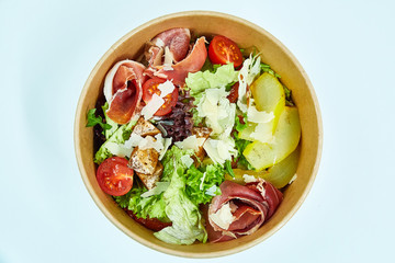 Salad with jamon, parmesan and feta cheese, cherry tomatoes, pear, lettuce, sun-dried tomatoes in a cardboard box