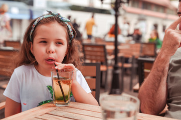 Happy little girl in a cafe on the street pb cocktail. Walking and eating outside.