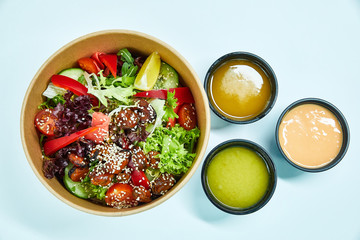 Salad with mussels and cherry tomatoes, red pepper, cucumber, lettuce, ginger, with a slice of lemon, decorated with sesame seeds in a cardboard box