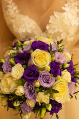 Close-up of cropped frame, the bride in a cream dress holds her wedding bouquet of yellow and purple roses, shows flowers to the camera. Wedding day, bridal bouquet.