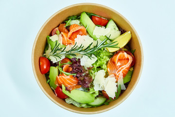 Salad with salmon and cherry tomatoes, lemon, avocado, cucumber, lettuce, arugula, Parmesan cheese, a sprig of rosemary in a cardboard box