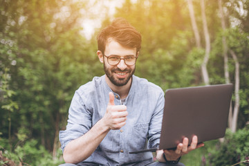 Freelance work concept. Businessman sitting on green grass and using laptop computer. Bearded man working with computer in park at sunny day. Outdoors nature journey and relaxation.