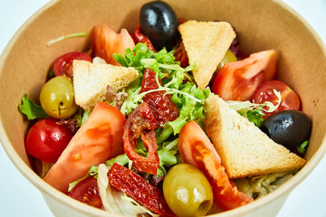 Vegetable salad with tomatoes, cherry tomatoes, sun-dried tomatoes, lettuce, olives, white bread crackers in a cardboard box