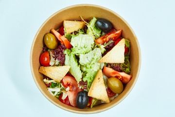 Vegetable salad with tomatoes, cherry tomatoes, sun-dried tomatoes, lettuce, olives, white bread crackers in a cardboard box