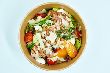Salad with grilled pork, parmesan cheese, cherry tomatoes, lettuce, arugula, quail eggs, persimmon, a sprig of rosemary in a cardboard box