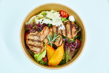 Salad with grilled pork, parmesan cheese, cherry tomatoes, lettuce, arugula, quail eggs, persimmon, a sprig of rosemary in a cardboard box