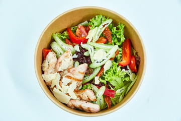 Salad with grilled chicken, parmesan cheese, cherry tomatoes, sun-dried tomatoes, lettuce, red pepper, celery in a cardboard box