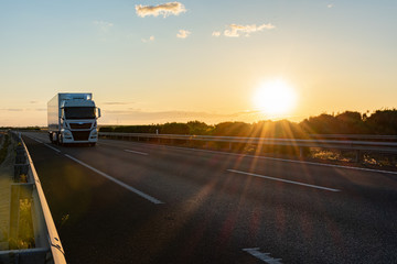 Truck with refrigerated semi-trailer driving on a highway with the sun low in the evening.