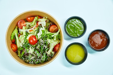 Vegetable salad with cherry tomatoes, cucumber, lettuce, arugula, asparagus beans and sesame seeds in a cardboard box