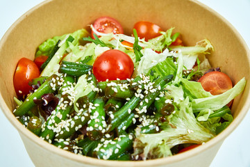 Vegetable salad with cherry tomatoes, cucumber, lettuce, arugula, asparagus beans and sesame seeds in a cardboard box