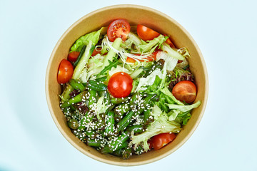 Vegetable salad with cherry tomatoes, cucumber, lettuce, arugula, asparagus beans and sesame seeds in a cardboard box