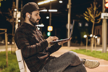 attractive young businessman working on startup sitting with laptop on the street. Freelance work concept.