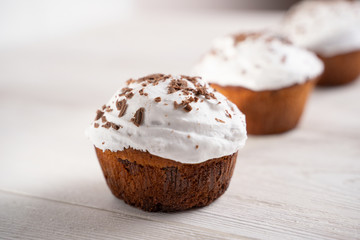 Cupcakes with whipped cream and chocolate chips on a white wooden table. Image for the menu or catalog of confectionery products.