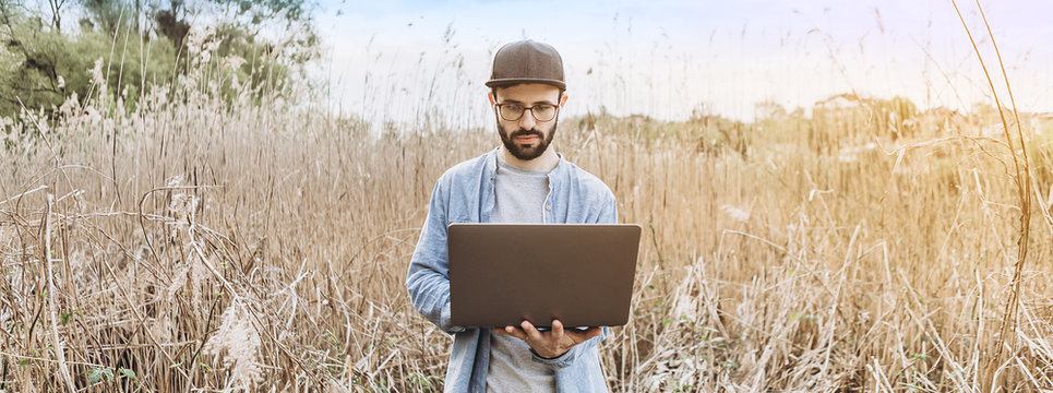 handsome bearded man in glasses freelancer working on a laptop outdoors in the mountains. Freelance concept