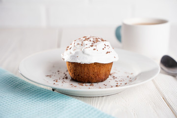 Cupcakes with whipped cream and chocolate chips on a white plate and a Cup of coffee in the background, on a white wooden table. Image for the menu or catalog of confectionery products.