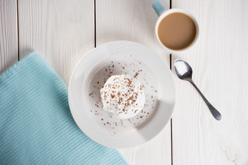 Cupcakes with whipped cream and chocolate chips on a white plate and a Cup of coffee in the background, on a white wooden table. Image for the menu or catalog of confectionery products.