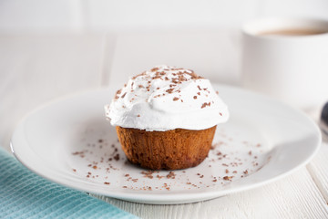 Cupcakes with whipped cream and chocolate chips on a white plate and a Cup of coffee in the background, on a white wooden table. Image for the menu or catalog of confectionery products.