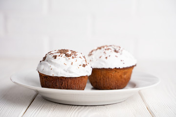 Cupcakes with whipped cream and chocolate chips on a white plate, on a white wooden table. Image for the menu or catalog of confectionery products.