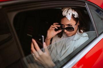 A beautiful caucasian businesswoman with a phone in her hand sits in a red car