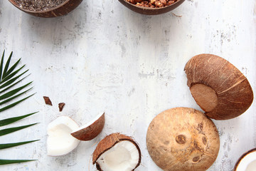 Pieces of coconut and leaves of a tropical tree on a light textured background. Horizontal photo. Copy of the space.