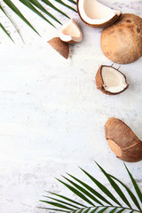 Broken coconut and tropical tree leaves on a light textured background. Copy of the space. Top view. © Alla