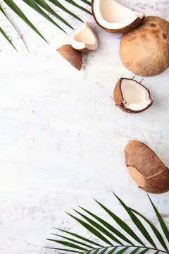 Broken coconut and tropical tree leaves on a light textured background. Copy of the space. Top view.