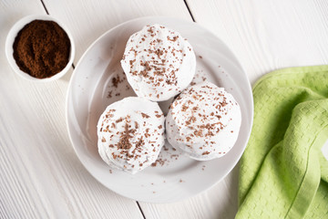 Cupcakes with whipped cream and chocolate chips on a white plate and a Cup of coffee in the background, on a white wooden table. Image for the menu or catalog of confectionery products.